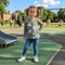 Child standing on a playground wearing a green shirt with cartoon designs and blue jeans.