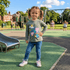Child standing on a playground wearing a green shirt with cartoon designs and blue jeans.