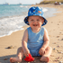 Child wearing a blue sun hat with boat pattern on a sandy beach.