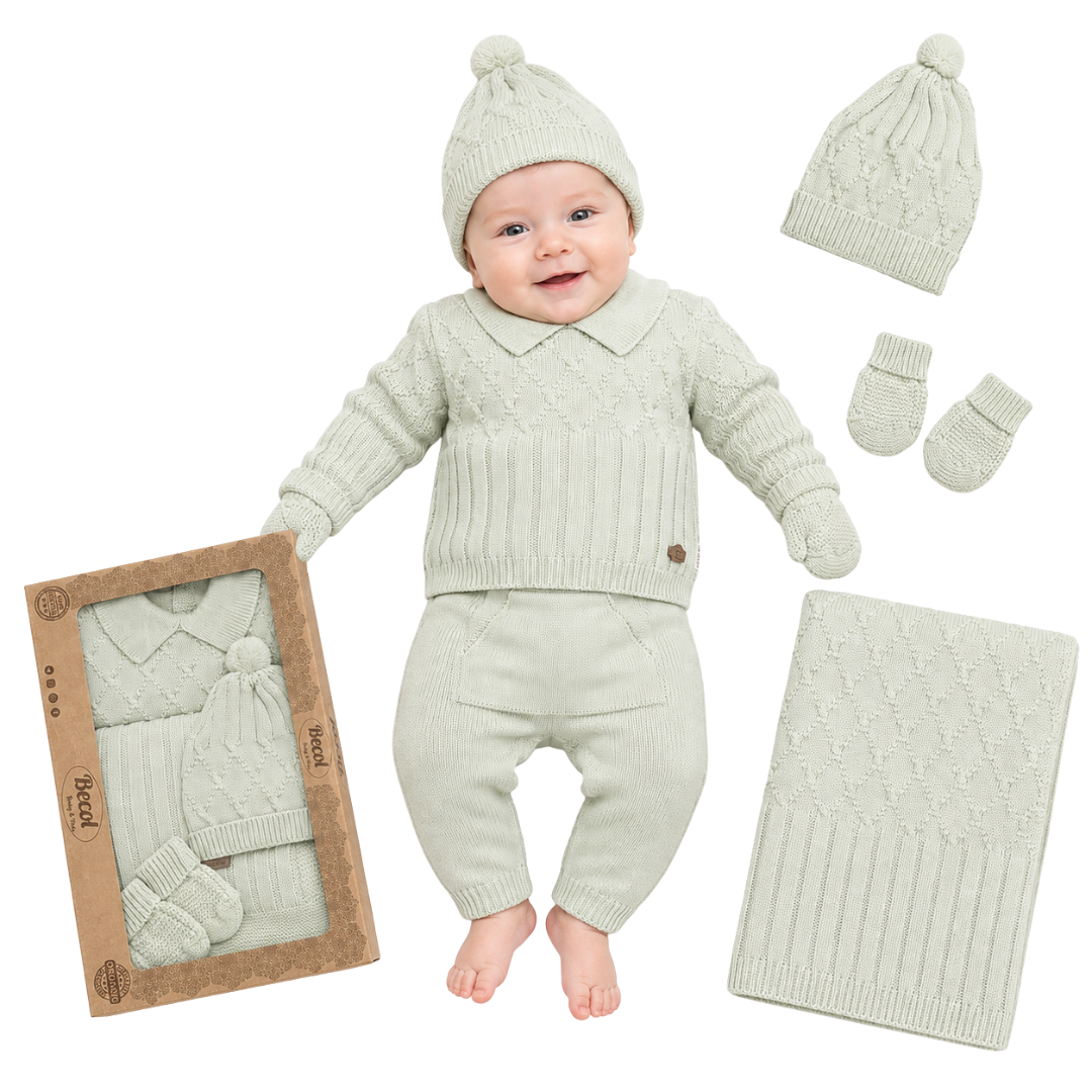 A baby wearing a light sage green knit three-piece outfit with a matching beanie and mittens, shown alongside the outfit packaging, a folded blanket, and additional accessories on a white background.