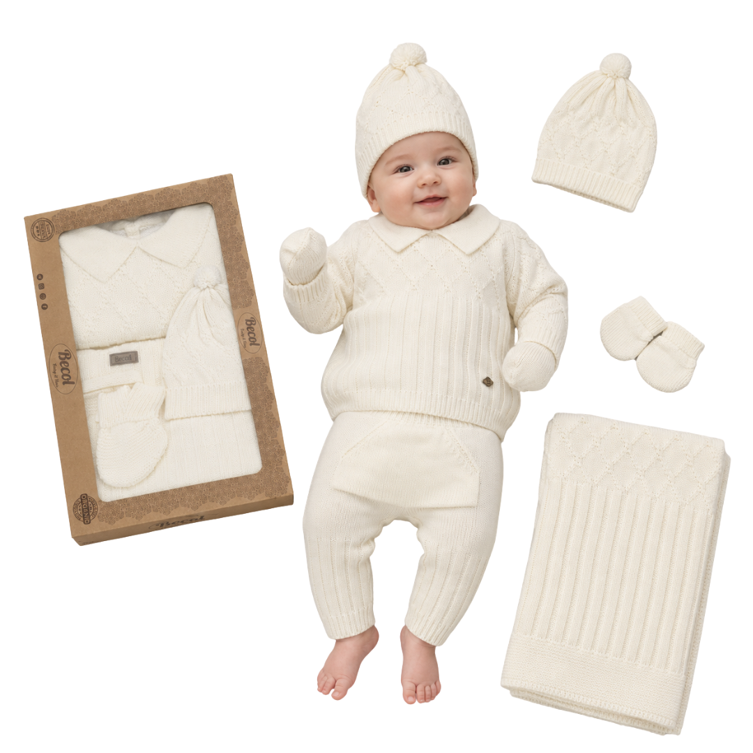 A baby wearing a cream-colored ribbed knit outfit set, including a hat with pom-pom, long-sleeve top, pants, and booties, shown next to the matching gift box and folded blanket on a white background.