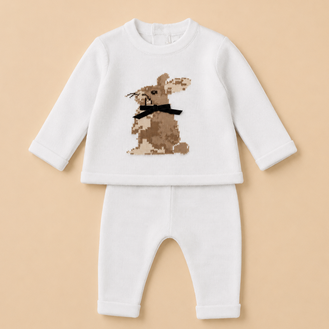 A baby two-piece outfit consisting of a white long-sleeve top and matching white pants, featuring a brown rabbit graphic with a black bow tie on the chest, displayed on a solid beige background.