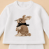 A white long-sleeve baby sweater featuring a pixelated brown rabbit graphic with a black bow tie on the chest, displayed against a solid beige background.