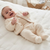 A baby lying on a white quilted mattress, wearing a cream-colored fleece footed sleeper with a matching buttoned cardigan.