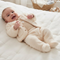 A baby lying on a white quilted mattress, wearing a cream-colored fleece footed sleeper with a matching buttoned cardigan.
