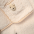 Close-up of a soft, beige fabric with a small bear toy inside a pocket.