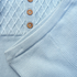 Close-up of a light blue knit garment showing a ribbed collar, a textured diamond-knit yoke, and three brown buttons on a henley-style top.