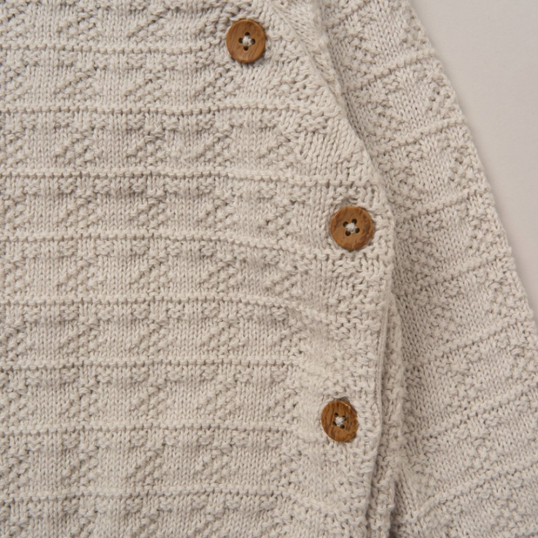 Close-up of a cream-colored textured knit cardigan featuring a diamond pattern and three wooden buttons.