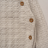 Close-up of a cream-colored textured knit cardigan featuring a diamond pattern and three wooden buttons.