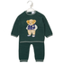 A dark green baby one-piece jumpsuit with a knitted teddy bear graphic on the chest, hanging on a clear plastic hanger against a white background.