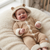 A baby wearing a beige knit hooded onesie with cream sherpa trim and bear ears on the hood, lying on a cream fleece blanket.