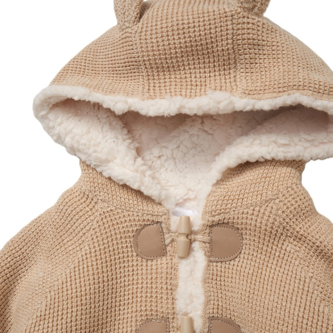 Close-up of a beige knit hooded jacket with a cream sherpa lining and tan toggle closures, shown against a white background.