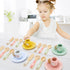 Child playing with a set of colorful toy cups and utensils on a white surface.