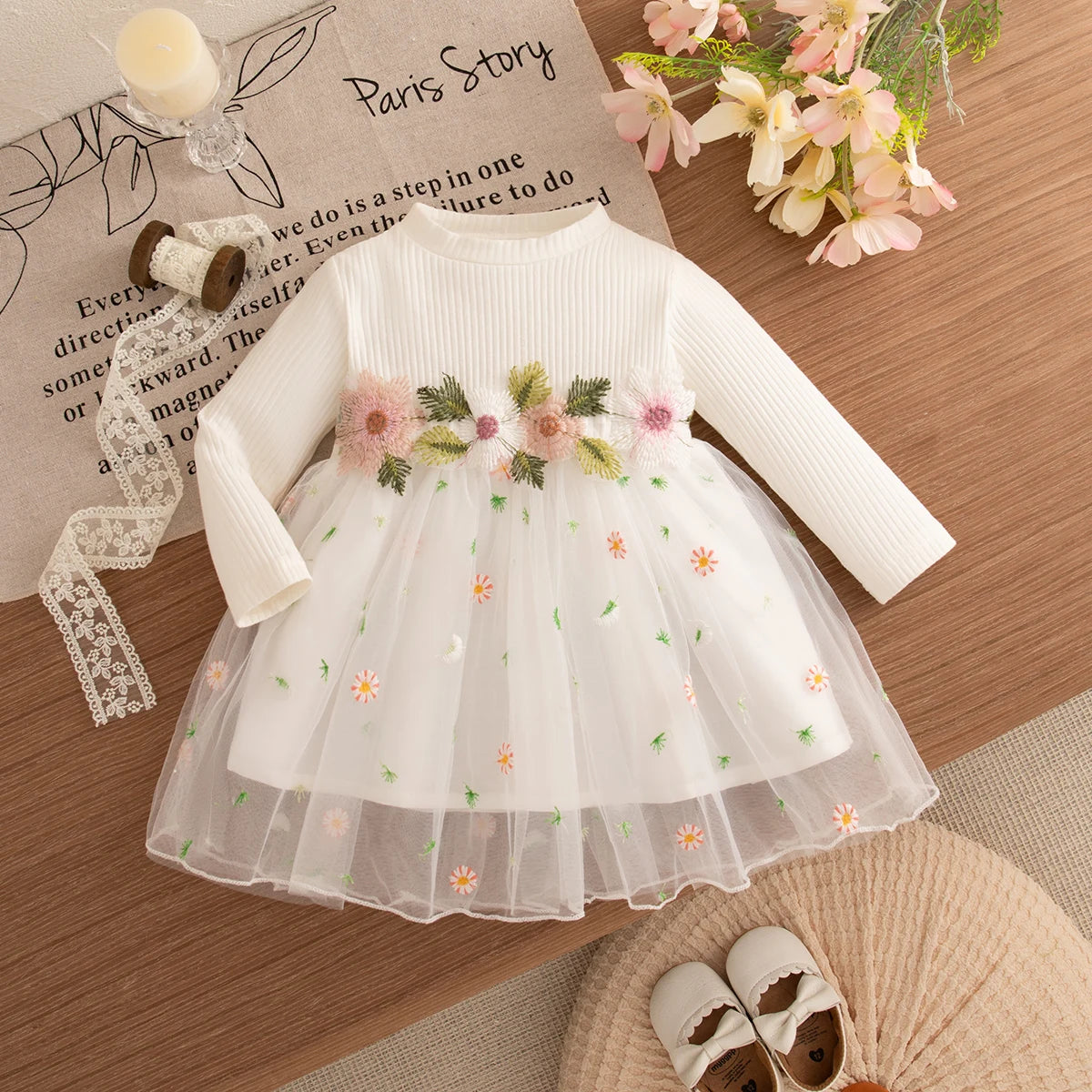 White dress with floral embroidery on a wooden surface with flowers and a candle.
