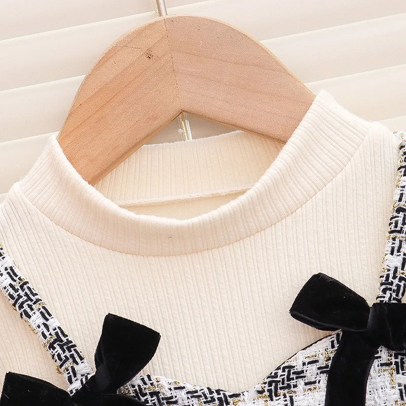 White sweater with black bow details on a wooden hanger against a white background