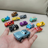 Collection of small toy cars on a light surface with a hand holding a blue car.