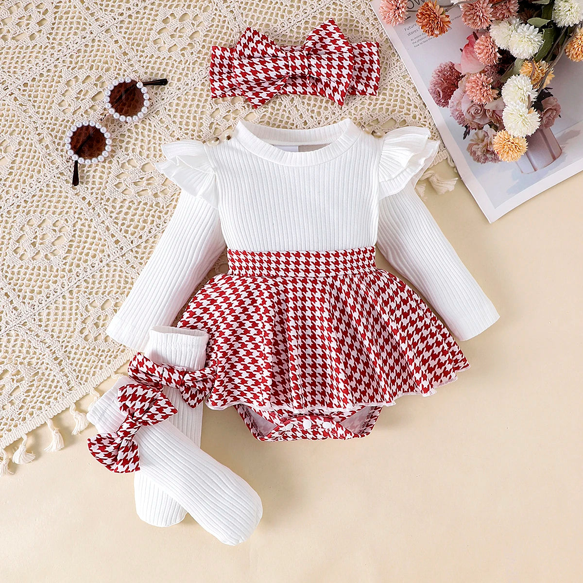 Baby outfit with white top, red and white checkered skirt, white tights, and headband on a textured surface.