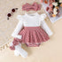Baby outfit with white top, red and white checkered skirt, white tights, and headband on a textured surface.