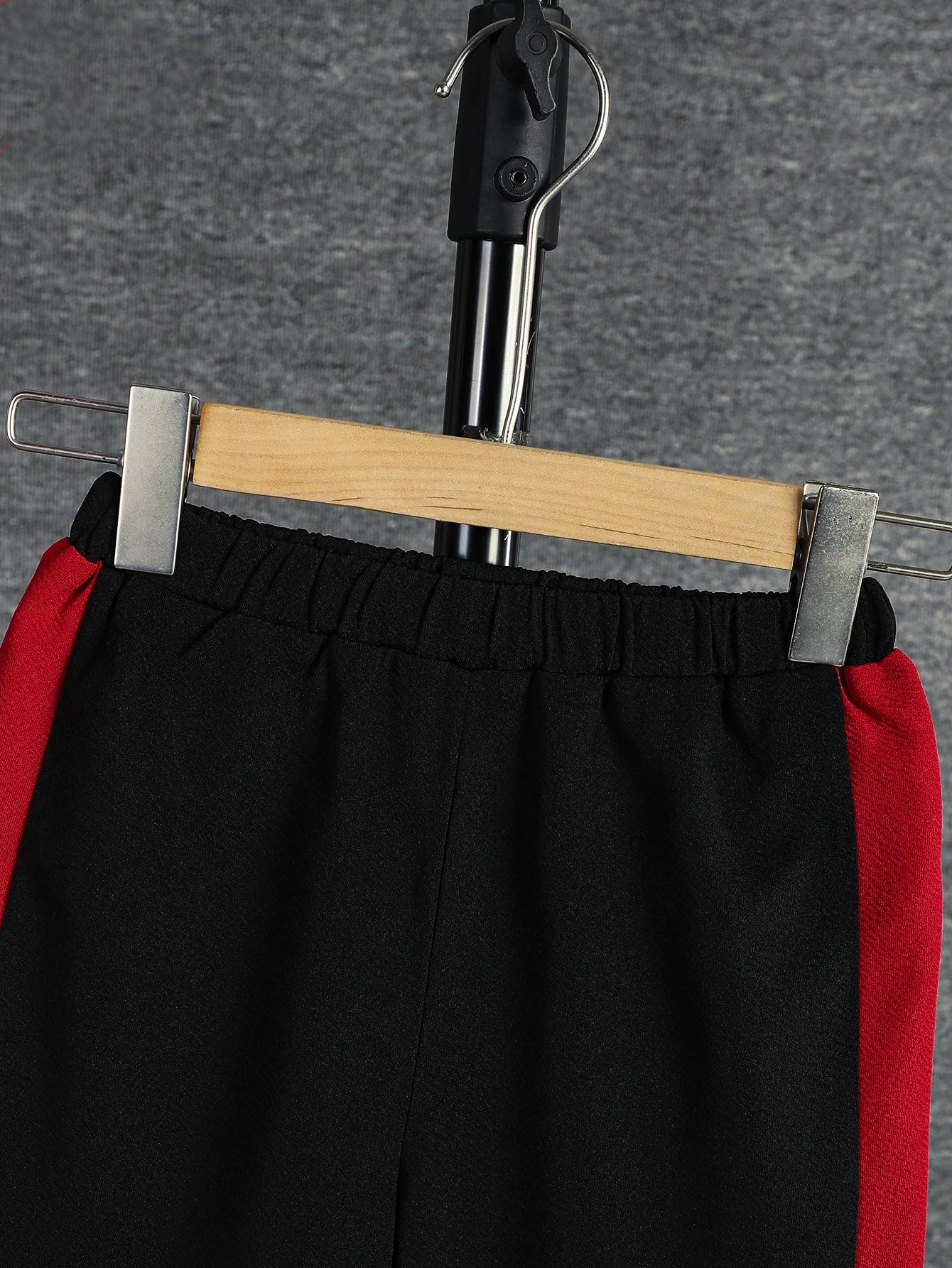 Black pants with red accents on a hanger against a gray background