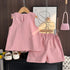 Pink children's outfit with shorts and a top on a hanger, with a small pink handbag and white shoes in the background.