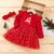 Red Christmas dress with reindeer design on a wooden surface, accompanied by a headband and small tree decorations.