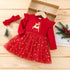 Red Christmas dress with reindeer design on a wooden surface, accompanied by a headband and small tree decorations.