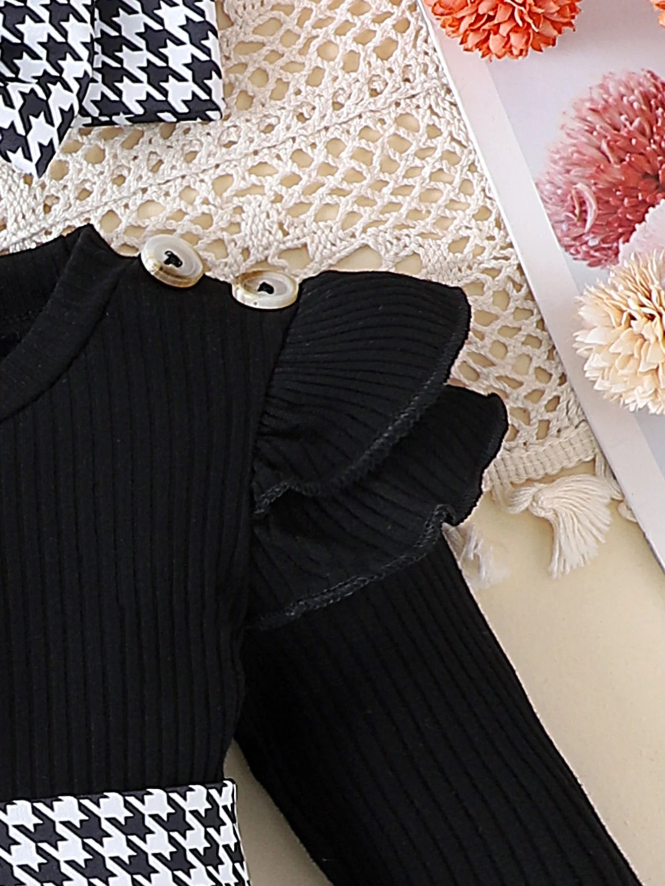 Black ribbed sweater with ruffled shoulders on a textured surface with flowers.