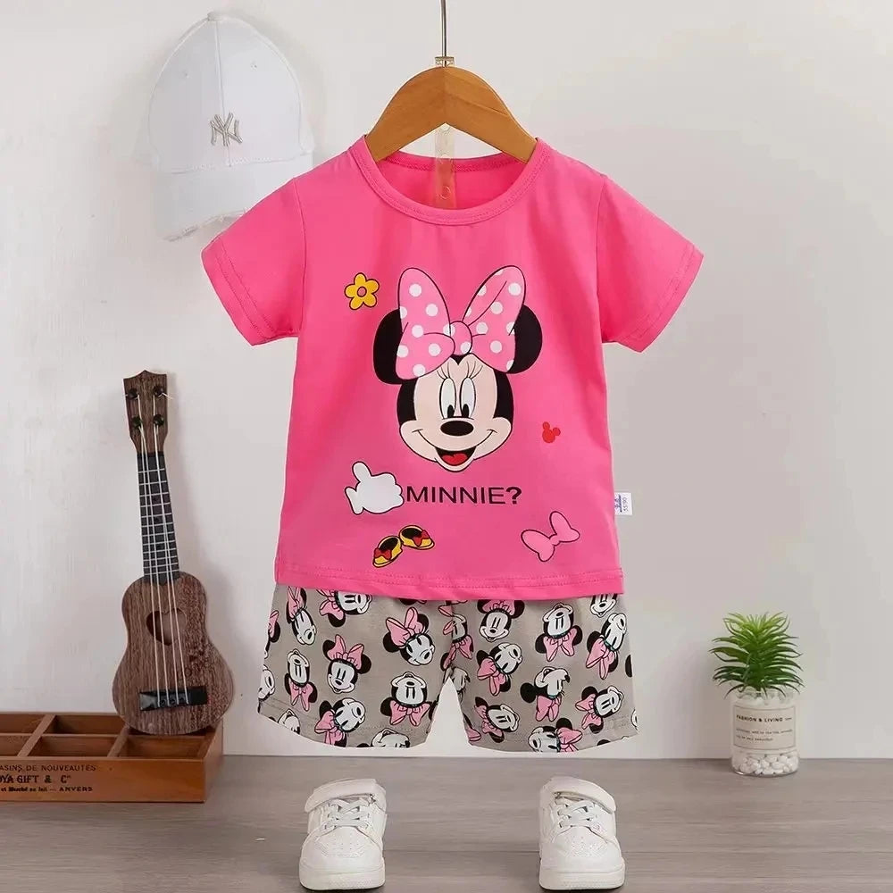 Pink t-shirt with Minnie Mouse design and gray shorts on a hanger against a white wall.