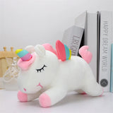 Plush unicorn toy with rainbow horn and pink hooves on a white surface with books in the background.