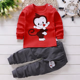 Red long-sleeve shirt with monkey graphic and gray pants on a wooden surface.