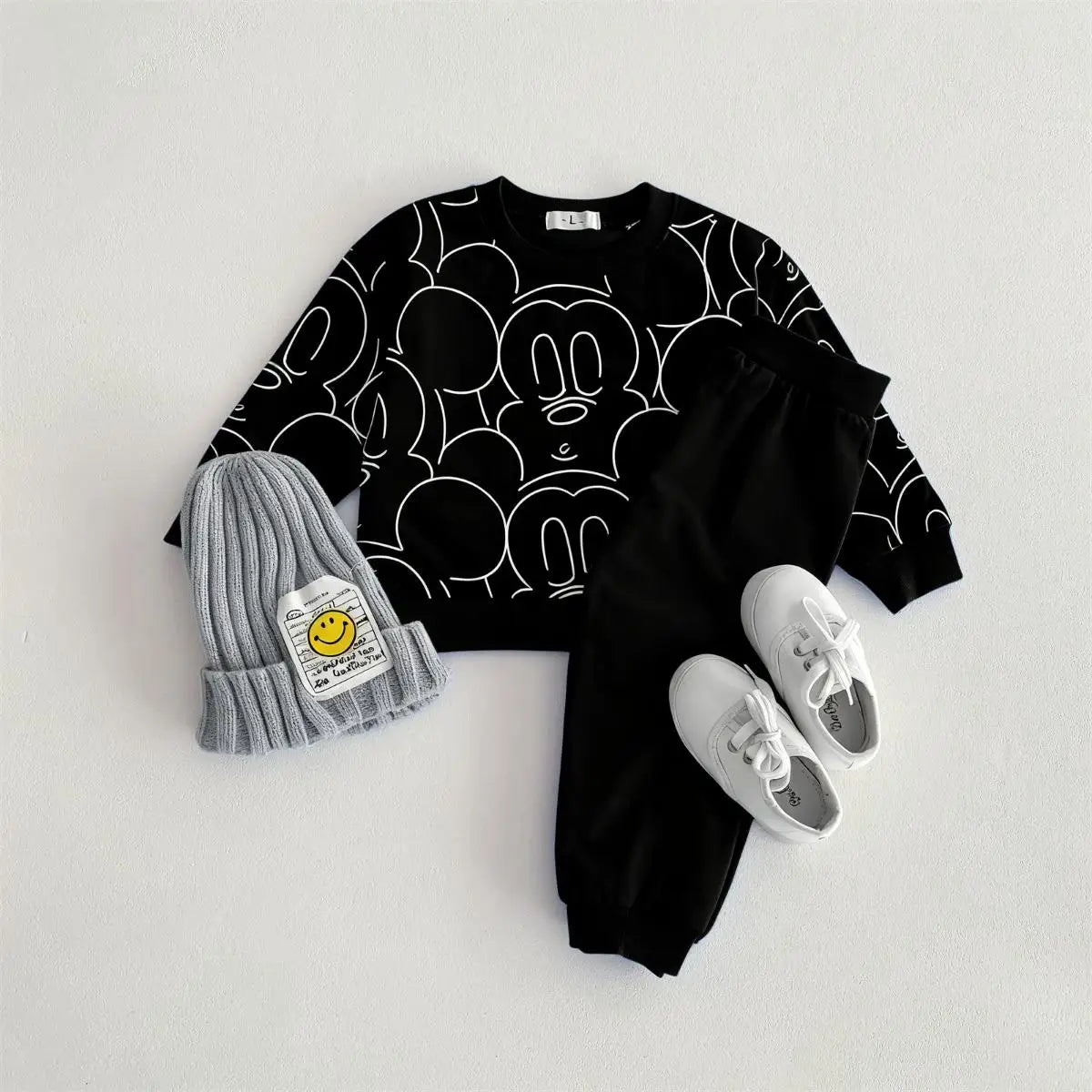 Black graphic t-shirt, gray beanie with smiley face, and white sneakers on a light gray background