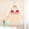 White dress with red bows on a hanger against a neutral background