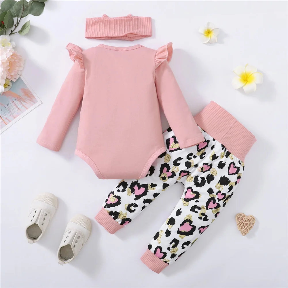 Baby outfit set with pink onesie, patterned leggings, and headband on a light background.