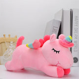 Pink unicorn plush toy with a rainbow horn on a white surface.