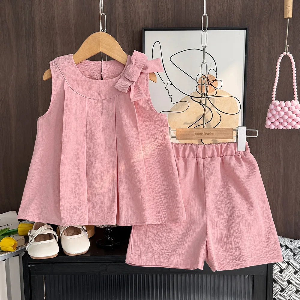 Pink children's outfit with top and shorts hanging on a wooden hanger against a wall with abstract art.