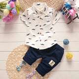 Children's outfit with white shirt and navy shorts on a wooden surface with decorative elements.