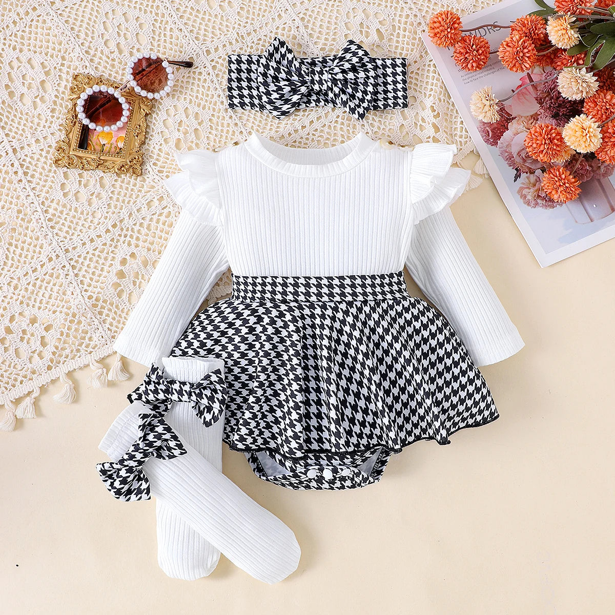 Baby outfit with white long-sleeve top, houndstooth pattern shorts, and headband on a textured surface.