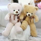 Two teddy bears, one beige and one white, sitting on a white surface.