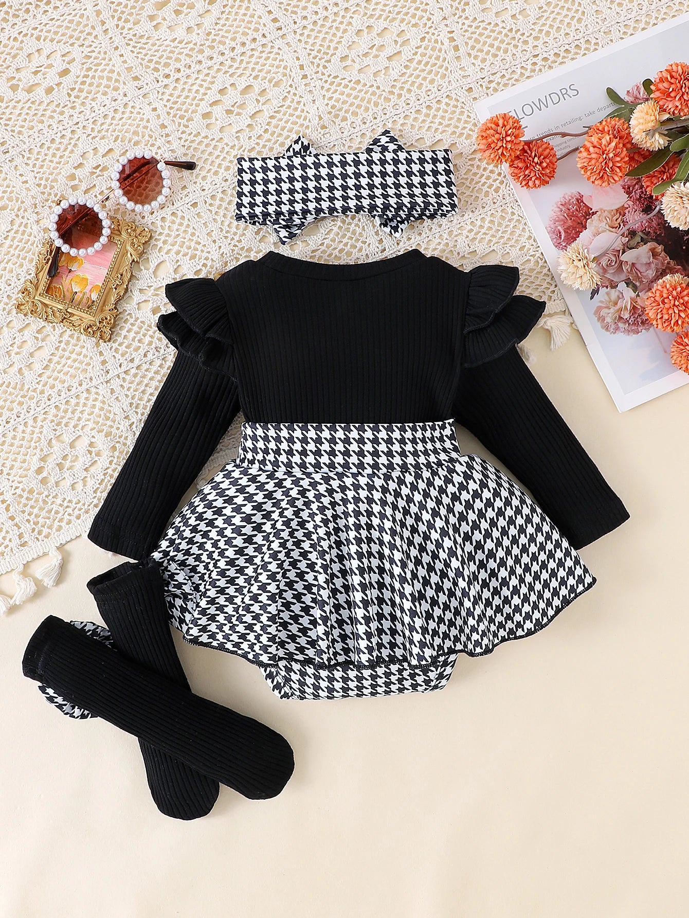 Black and white checkered romper with ruffled sleeves on a textured surface.