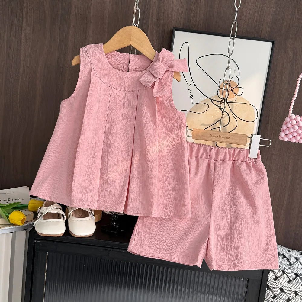 Pink children's outfit with a top and shorts on a hanger against a wooden wall.