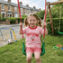 Young girl in a pink 'Cherry Cake Milk' shirt on a swing set in a residential area.