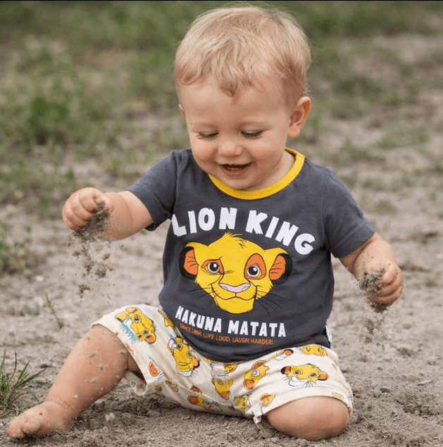 Child wearing a 'Lion King' shirt and shorts playing in the sand
