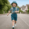 Child running on a street wearing a blue hat, floral shirt, suspenders, and shorts.