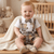 Baby wearing a plaid outfit with suspenders and a bow tie, sitting on a wooden floor.