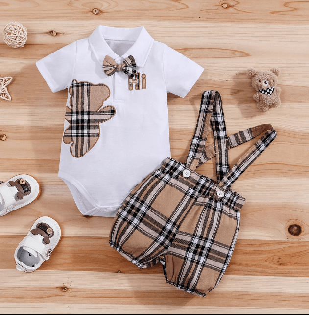Baby outfit with white shirt, brown bear design, plaid shorts, and suspenders on a wooden surface.