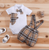 Baby outfit with white shirt, brown bear design, plaid shorts, and suspenders on a wooden surface.