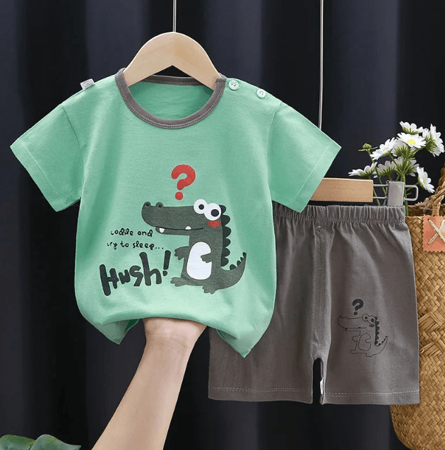 Children's green t-shirt with crocodile design and gray shorts on a hanger against a dark background.