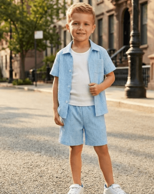 Young boy in light blue shirt and shorts standing on a street.