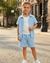 Young boy in light blue shirt and shorts standing on a street.