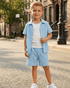 Young boy in light blue shirt and shorts standing on a street.